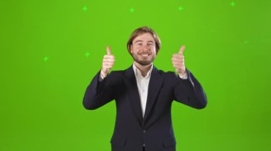 Stüdyoda poz veren mutlu, mutlu ve neşeli bir adam. Yakışıklı erkek, elini kaldırıyor, kameraya bakıyor, gülümsüyor. Yeşil stüdyo arka planında izole edilmiş..
