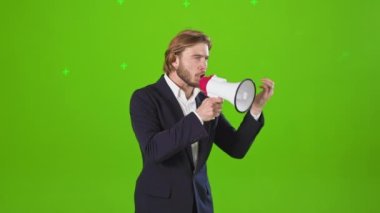 Stüdyoda elinde megafonla fotoşopu olan hatipin yan görüntüsü. Yakışıklı, kostüm ve gömlek giyen, ağlayan, duygusal genç bir erkek. Yeşil stüdyo arka planında izole edilmiş..