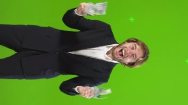 Para tutan heyecanlı adam stüdyoda kazandığı paradan dolayı mutlu. Erkek görüntüsü, bir tomar para sallayan, neşeyle gülümseyen, ağır çekimde. Para kavramı, başarı, şans.