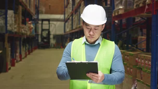 亚洲男性仓库管理员穿着安全帽和反光背心 在检查储物柜的组织结构时使用剪贴板做笔记 后勤改进和控制概念 — 图库视频影像