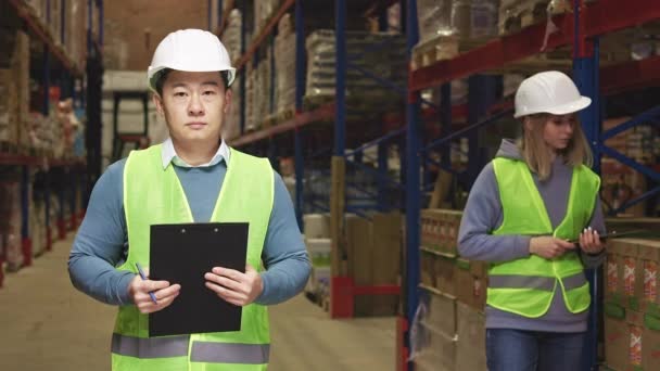 Serious Man Clipboard Hands Standing Spacious Warehouse Female Colleague Using — Stock Video