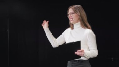 Kulaklığı ve panosu olan motive edici bayan danışman seminer sahnesinde duruyor ve esir seyirciyi karşılamak için heyecanla kolunu sallıyor. Ağ oluşturma, eğitim ve kariyer büyümesi kavramı.