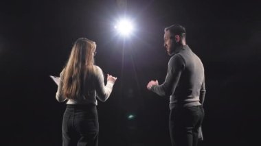 Gayriresmi iş koçlarının, konferans sırasında seyircilerle fikir alışverişinde bulunmaları. Beyaz erkek ve kadın siyah sahnede kulaklık ve dosya kullanıyor..