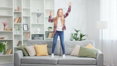 Rahat kıyafetler giymiş, rahat bir kanepede mutlu mesut zıplayıp boş aktivitelerin saf zevkini yaşayan küçük bir kız. Dinamik çocuk modern dairede harika vakit geçiriyor..