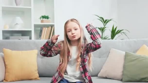 活泼活泼的孩子坐在舒适的沙发上 用手做着滑稽的动作 一个有着长发的艺术女孩 在时尚舒适的公寓里快乐地跳舞 — 图库视频影像
