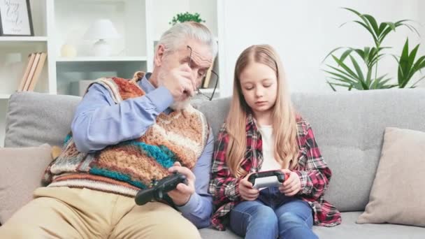 金发碧眼的聪明女孩教爷爷如何用操纵杆玩电子游戏 专心致志的祖父和孩子一起呆在家里 两代人的概念和无线技术 — 图库视频影像