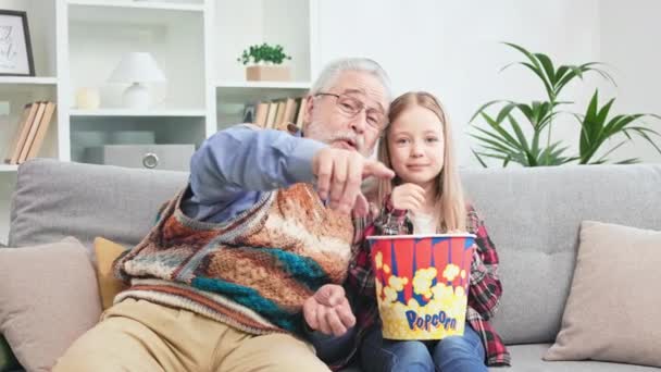 祖父母很快乐 孩子们在舒适的沙发上休息 一边欣赏喜剧电影 金发女郎拿着一大盒爆米花和爷爷一起吃饭 家庭在家时间的概念 — 图库视频影像