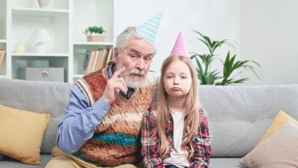 Portret Zdenerwowanego Dziadka Wnuka Siedzących Kanapie Rożkami Urodzinowymi Głowie Mała — Wideo stockowe
