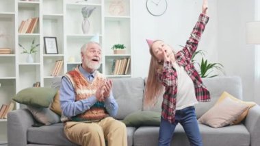 Eğlence düşkünü, emekli bir beyefendi koltukta oturup parti konileriyle torunlarının gösterisinden zevk alıyor. Mutlu büyükbaba genç yetenekleri alkışlarken neşeli sanatçı kız dans ediyor ve şarkı söylüyor..