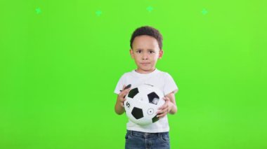 Stüdyoda futbol topu tutan sıradan kıyafetler giyen gülümseyen küçük çocuk. Yeşil arka planda izole edilmiş, topla poz veren Afro-Amerikan erkek çocuk manzarası. duygular, hobi konsepti.