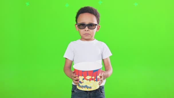 很酷的小男孩戴着太阳镜 手里拿着一大桶爆米花 工作室里还有零食 带着爆米花笑着的非洲裔美国小孩的前景色 对着相机笑着 被绿色隔离 休闲概念 — 图库视频影像