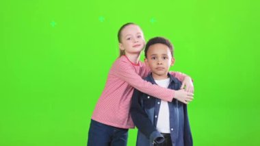 Beyaz saçlı güzel bir kız, at kuyruklu, Afrikalı Amerikalı bir çocuğa sarılıyor. Genç bir çocuğu kucaklayan kız arkadaşın ön görüntüsü, yeşilde izole edilmiş kameraya bakarken. Arkadaşlık kavramı.