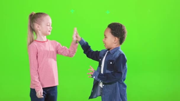 快乐的高加索女孩和非洲裔美国小男孩拍手 在演播室里击掌击掌 一边看孩子们手拉手玩耍一边笑 孤零零地躺在绿色上 童年的概念 — 图库视频影像