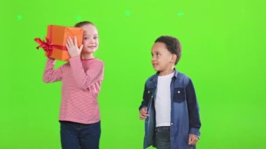 Afrika kökenli Amerikalı bir erkek onu izlerken, Kafkasyalı bir kız hediye kutusunu sallıyor. Mutlu çokkültürlü çocukların hediyelerden zevk almaları, kutlama yapmaları, yeşilde soyutlanmaları ön planda. Kutlama konsepti.