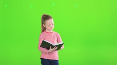 Güzel küçük kız ilginç bir kitap okuyor ve kameraya gülümsüyor, hareket halinde. Atkuyruklu, atkuyruklu şirin bir kız çocuğu stüdyoda dikilirken görülüyor. Eğitim kavramı.