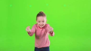 İçeride kameraya açıklarken aktif olarak el kol hareketi yapan heyecanlı bir bayan çocuk. Şirin küçük kız konuşuyor, el sallıyor, stüdyoda dikilirken, yeşil arka plan, hareket. Duygu kavramı.