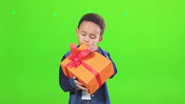 好奇的小男孩看着大大的节日礼品盒 猜猜看里面是什么 穿着衬衫的非洲裔美国男孩的正面照片 他们抱着礼物 被绿色隔离 庆祝概念 — 图库视频影像