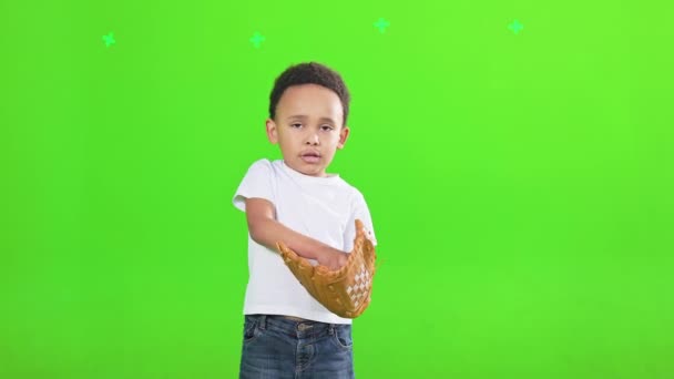 年轻的非洲裔美国男孩 戴着棒球和皮手套 练习在室内抛掷和接球 集中的男孩棒球手的正面视图 隔离在绿色工作室的背景 体育概念 — 图库视频影像