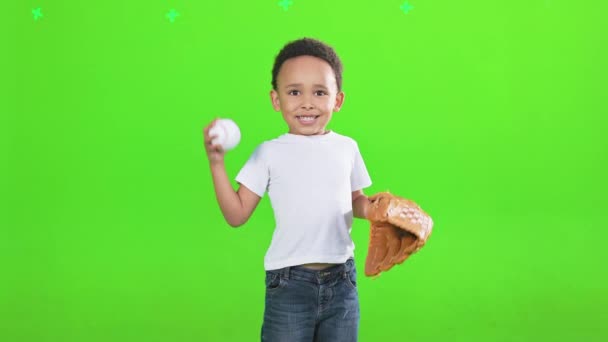 值得称道的非洲裔美国男孩与棒球手套扔球在工作室前面 眼前是一个笑着的小男孩打棒球的场景 被绿色的背景隔开了 体育的概念 — 图库视频影像