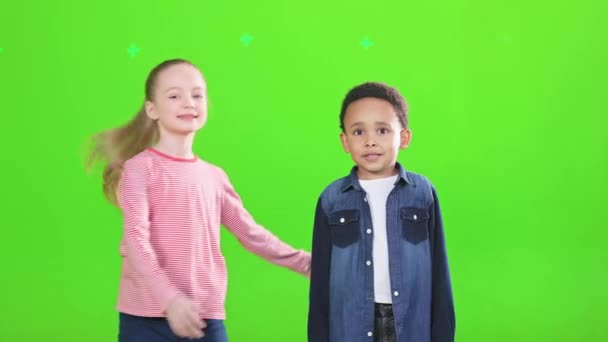 有趣的高加索女孩跳 接近可爱的非洲裔美国男孩 眼前的孩子们幸福的朋友拥抱着 一边对着相机笑 一边孤零零地躺在绿色上 友谊概念 — 图库视频影像