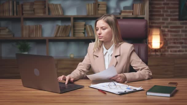 在温暖舒适的工作环境中 穿着正式衣服的严肃女人坐在现代化的办公桌前 在笔记本电脑上打字 可敬的女商人核查文件中规定的信息 — 图库视频影像