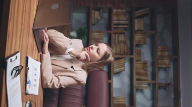 Kişisel bilgisayara bakıp piyasa araştırması yapan genç yöneticinin dikey videosu. Şık bir ceket giymiş odaklanmış kadın iş yerinde beyin fırtınası yapıyor ve düşünceli bir çeneye dokunuyor..