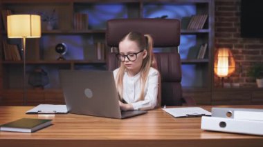 Ciddi yüz ifadesi olan, uzun tahta masaüstünde oturan ve taşınabilir bilgisayarda yazan küçük bir bayan profesyonel. Web sitelerinde yararlı bilgiler arayan at kuyruklu çocuk odaklı.