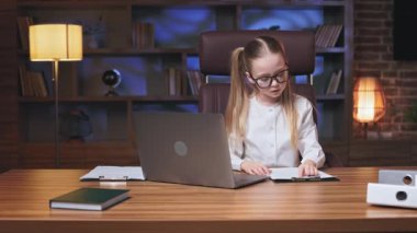 Küçük bir ofis çalışanı bilgisayardan finansal rapor yazıyor ve belgeleri doğruluyor. Çağdaş ofis odasında çalışan ve çevrimiçi işler için modern teknolojileri kullanan çalışkan çocuk..