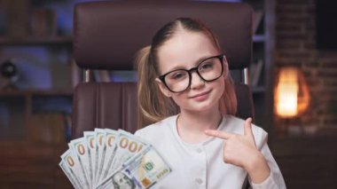 Elinde bir tomar banknot tutan ve kameraya bakan mutlu reşit olmamış kız portresi. Altın saçlı, iki at kuyruklu, parmakla parmakla gösterilen ve zevk veren bir çocuk..