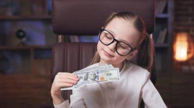 Rahat, huzurlu, beyaz bir çocuk rahat bir ofiste yönetici koltuğunda dinleniyor ve yavaşça dolar banknotlarının hayranını sallıyor. Sevimli liseli kız kameraya bakıyor ve nazikçe gülümsüyor..