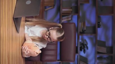 Sevgili küçük kızın aile işlerinde en sevdiği pelüş oyuncakla oynadığı dikey video. Hayalperest çocuk kedi yavrusuyla konuşuyor, sarılıyor ve ikisi de dizüstü bilgisayarla oynuyor..