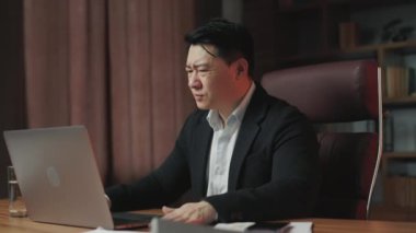 Resmi kıyafet giyen Asyalı bir adamın ofis işyerindeki veri kaybıyla ilgili sorunları olduğuna dair bir bakış açısı. Kafası karışmış bir beyefendi stresli, dokunaklı ve bilgisayarı kapatıyor..