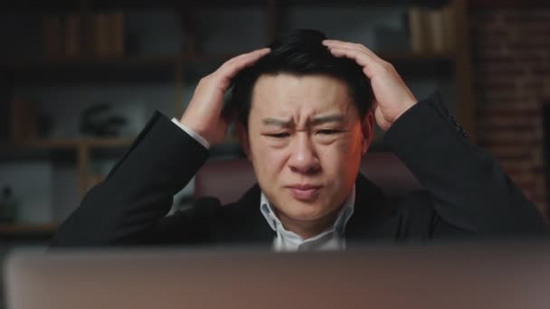 快適なオフィスチェアに座って 最新のビジネスニュースを読むアジアの紳士のクローズアップ 手で頭に触れ コンピュータを閉じて 強い失望を感じる金融マネージャーを動揺 — ストック動画