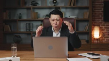 Stresli Asyalı CEO şirket iflasıyla ilgili tebligat alıyor ve umutsuzca hayır diye bağırıyor. Hayal kırıklığına uğramış bir adam dizüstü bilgisayara bakıyor, kafasını tutuyor ve inkar ederken el sallıyor..
