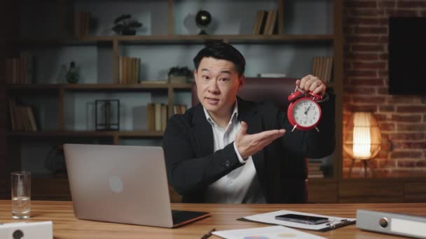 パーソナルコンピュータや携帯電話で長い木製のテーブルに座ってアジアの従業員のフロントビュー 黒スーツの幸せな男は赤い時計を示していますその作業時間が終了し オフィスを離れることを意味 — ストック動画