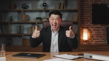 Beyaz gömlekli ve resmi siyah takım elbiseli heyecanlı Asyalı girişimci ofis koltuğunda otururken iş başarısıyla övünüyor. Gururlu adam parmağını kaldırıyor ve kendini işaret ediyor..