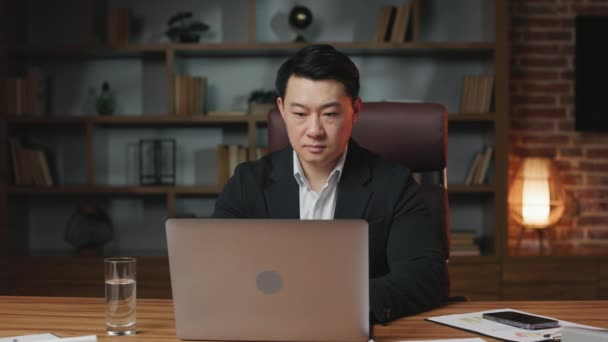 勤勉なアジアの専門家は オフィスでの仕事を完了し ポータブルラップトップをシャットダウンします 木製のデスクトップから立ち上がって職場を離れる中年の男 — ストック動画