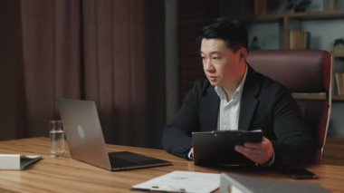İş kıyafetleri içinde ciddi bir şirket CEO 'su çağdaş ofis alanında kalırken video üzerinden çalışanla konuşuyor. Odaklanmış Asyalı girişimci taşınabilir bilgisayar kullanarak şirket sorunlarını tartışıyor.