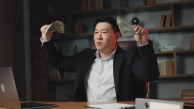 Komik Asyalı milyoner elleri para dolu ritmik hareketler yapıyor. Başarılı finans direktörü ofisteki masaüstünde oturan büyük şirket gelirini gösteriyor..