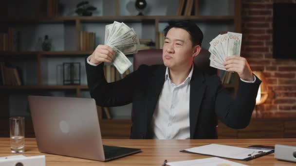 手元に数百ドルを保有し 顔の前で資金を調達する誇りあるビジネスエグゼクティブ 暗髪のアジア人男性は 仕事でリモートコンピュータでデスクトップに座って繁栄を楽しんでいます — ストック動画