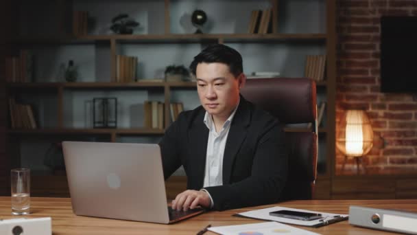 アジアのオフィス従業員は 居心地の良い職場でパーソナルコンピュータにタイプする深刻な顔の表現をしています 赤い手動時計を取って時を指すスーツの黒髪の男 — ストック動画