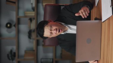 İş yerinde kolları dizüstü bilgisayarın önünde x üreten resmi giyinmiş endişeli bir iş adamı. Ofisteki teknik sorunlar yüzünden Asyalı kızgın profesyonel kayıp. Dikey video.