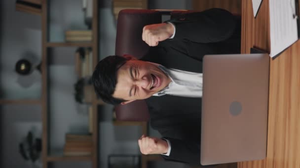 积极的亚洲成年人坐在写字台前 与工作的计算机一起表演优胜舞蹈的垂直视频 庆祝期待已久的爬上公司阶梯的快乐商务人士 — 图库视频影像