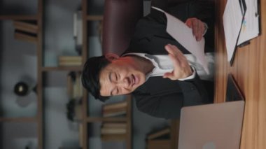 Öfkeli Asyalı yönetici iş yerindeki bilgisayar kamerasıyla sanal toplantı sırasında kağıt kayıtlarını yırtıyor. Saldırgan işveren kovulma tehdidiyle parçalarını havaya fırlatıyor. Dikey video.