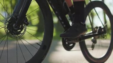 Kırsal alanda, kaldırımlı garaj yolu boyunca yavaş adımlarla pedal çeviren erkek bisikletinin yakın çekim görüntüsü. Yazın açık havada bisiklet sürmenin sağlığa faydalarından yararlanan genç kaslı profesyonel.