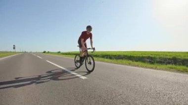 Tam donanımlı odaklanmış erkek, hızlandıktan sonra motorun üzerinde ayakta durarak pozisyonunu değiştiriyor. Spor kıyafetli deneyimli bir sürücü yazın temiz yolda bisiklet egzersizi yapıyor..