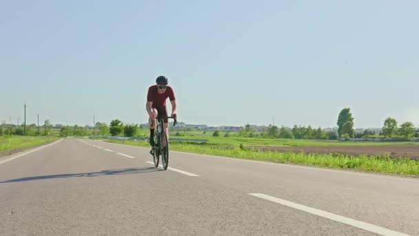 年轻的职业自行车手穿着运动服骑着美丽的乡村小路穿过田野 在阳光明媚的夏日进行力量锻炼的同时 有运动能力的成年人提倡积极的生活方式 — 图库视频影像