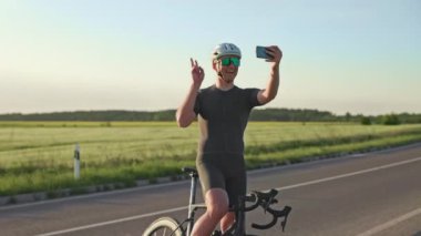 Şen şakrak bisiklet sürücüsü gün batımında tarlaların arasında dikilirken akıllı telefondan video görüşmesi yapıyor. Keyifli sporcular internette arkadaşlarıyla kırsal eğitim deneyimleri hakkında sohbet ediyorlar..