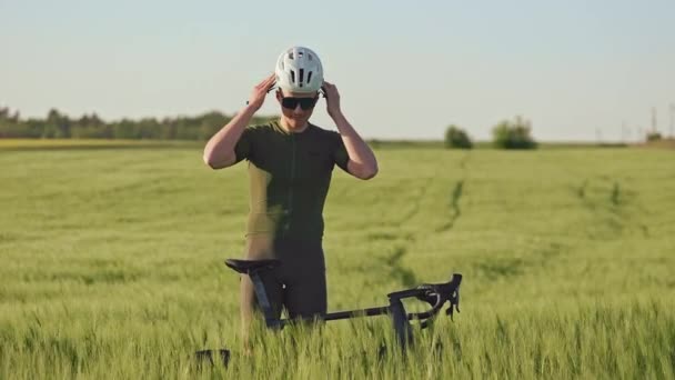 年轻运动员站在绿地的公路自行车旁 头戴白色防护头盔的全景 专业自行车手在夏天从与环境的互动中获得好处 — 图库视频影像
