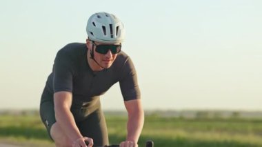 Spor kıyafetli sağlıklı bir erkeğe odaklan gün batımında asfalt yolda bisiklet sür. Dayanıklılık eğitimli sporcu, kilometrelerce mesafeyi rahatça kat ederken rahat sürüş pozisyonunu koruyor..